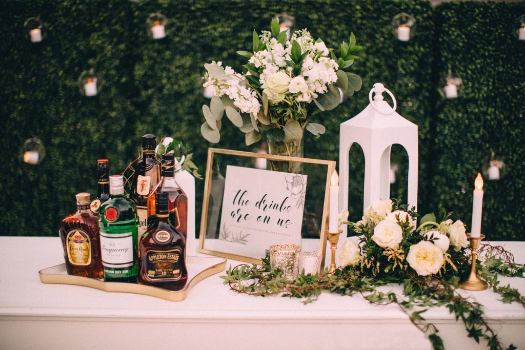 Custom signage and assortment of top-shelf liquors surrounded. by green florals