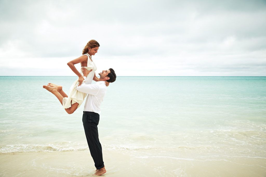 Groom lifts bride at the ocean's edge.