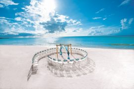 Beachfront destination wedding location depicts a ceremony setup with chair arranged like a seashell