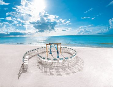 Beachfront destination wedding location depicts a ceremony setup with chair arranged like a seashell