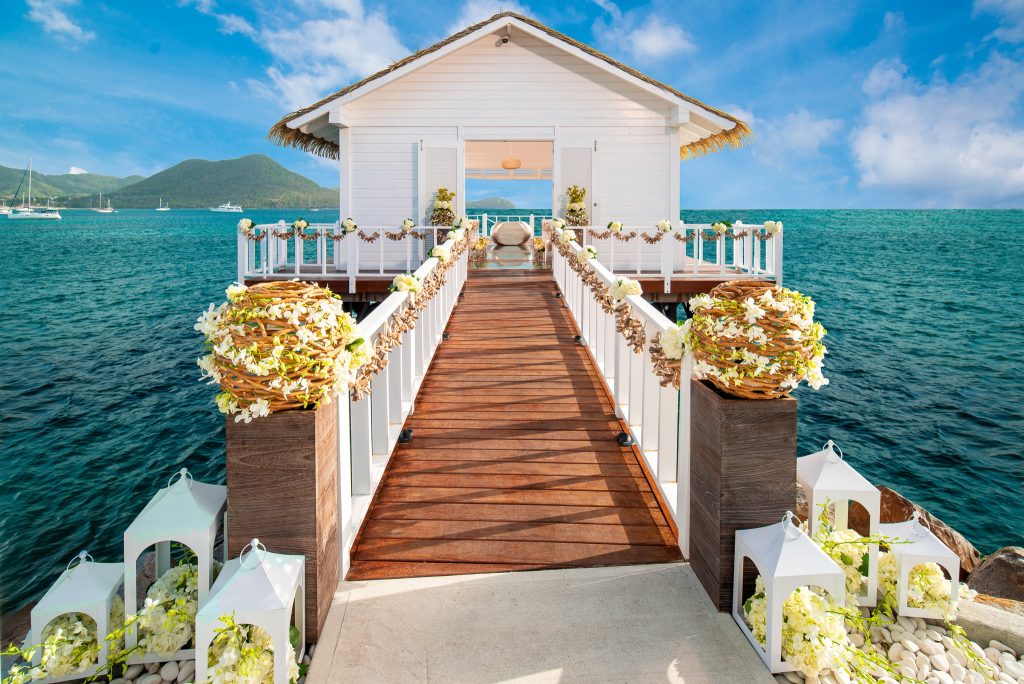 Bridge leading up to an over-the-Water wedding chapel, surrounded by blue waters and mountains looking on in the background.