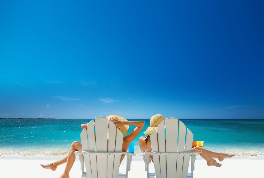 Best friends lounging in Adirondack chairs, oceanside. 