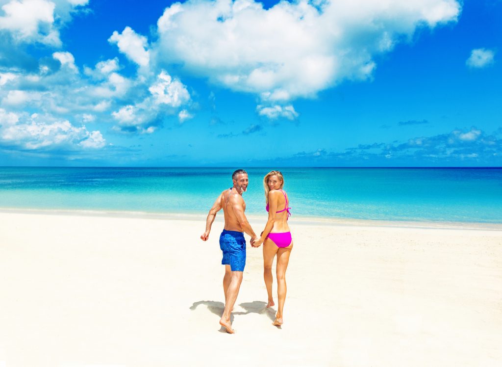 Couple walks toward crystal blue waters on a white sand beach