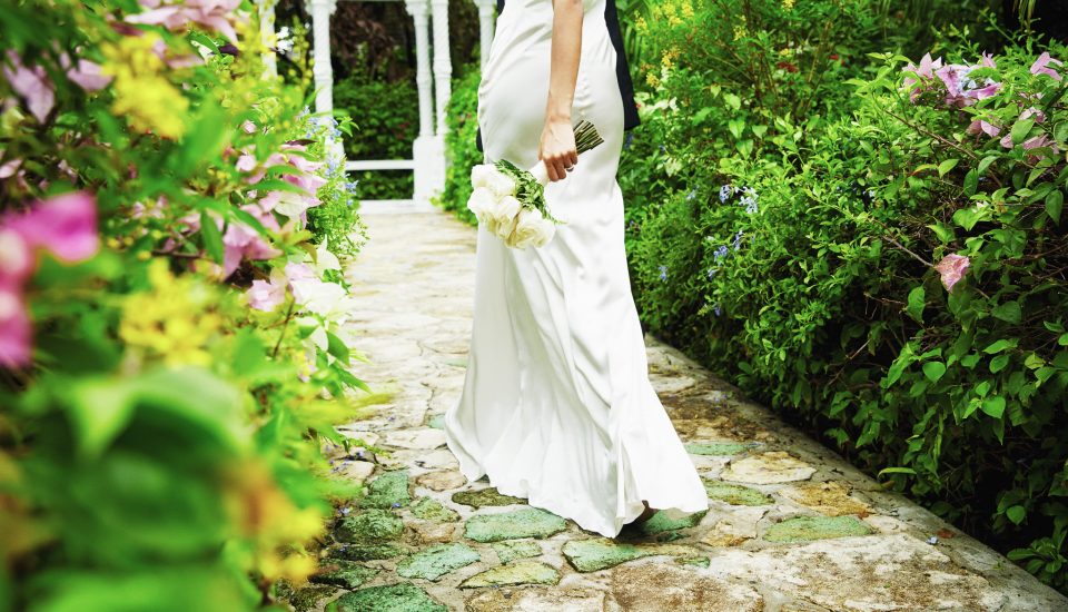 Bride walking through a lush garden, holding a posy wedding bouquet.